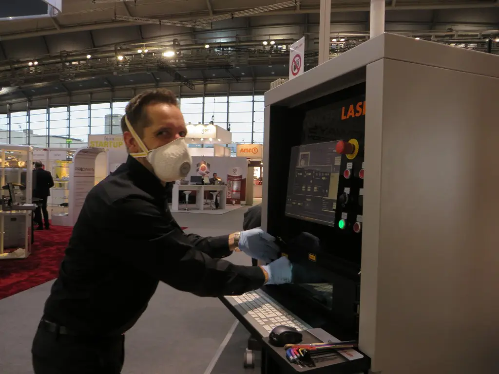 Bij het werken met metaalpoeders zijn persoonlijke beschermingsmiddelen belangrijk. Op de stand van Concept Laser werd een goed voorbeeld gegeven: machine open dan handschoenen aan en snuitje voor